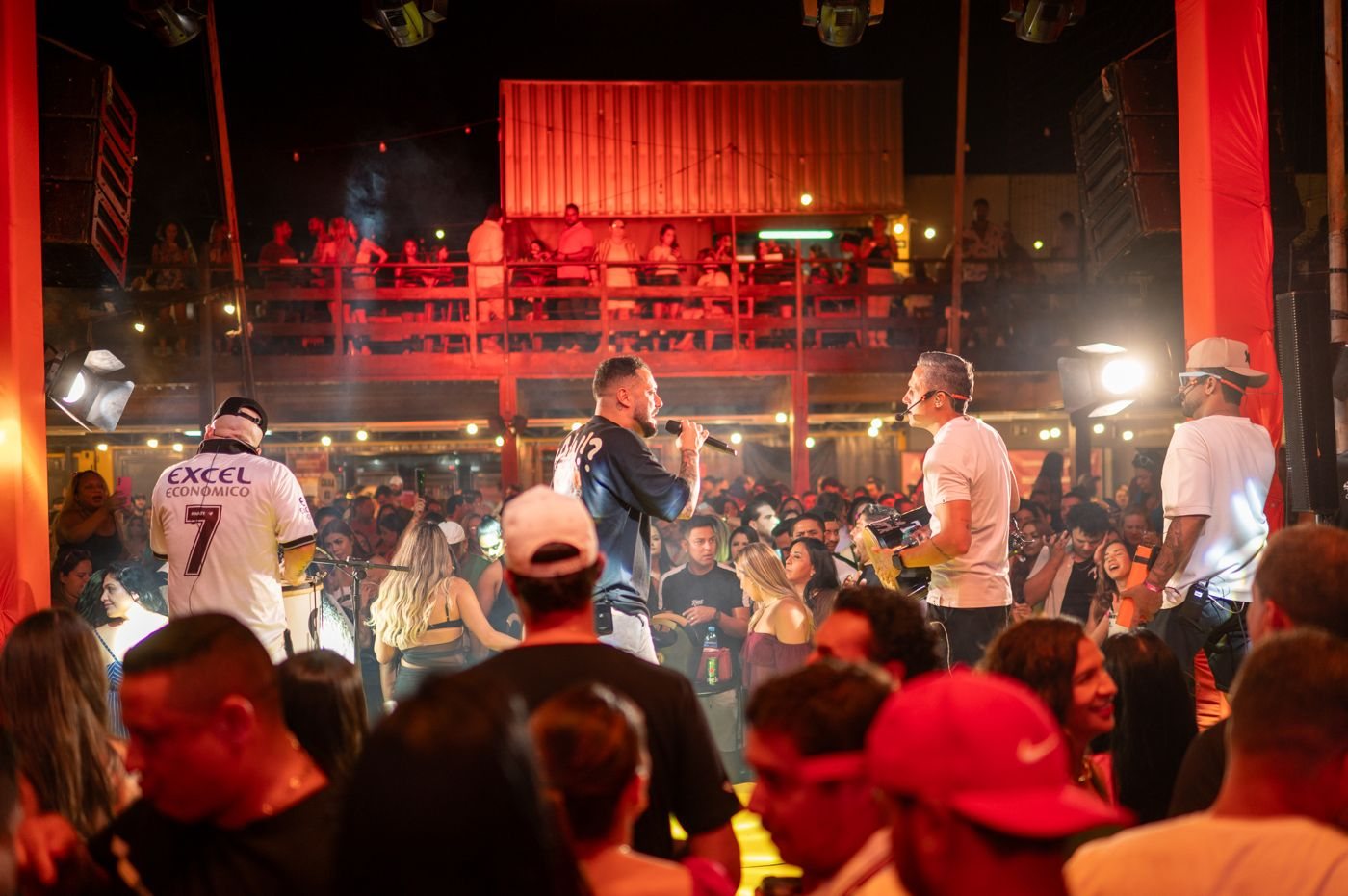 O Samba10 no palco, cantando pra uma casa lotada sob luz vermelha.